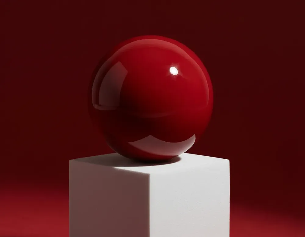 A glossy red sphere on a white cube
